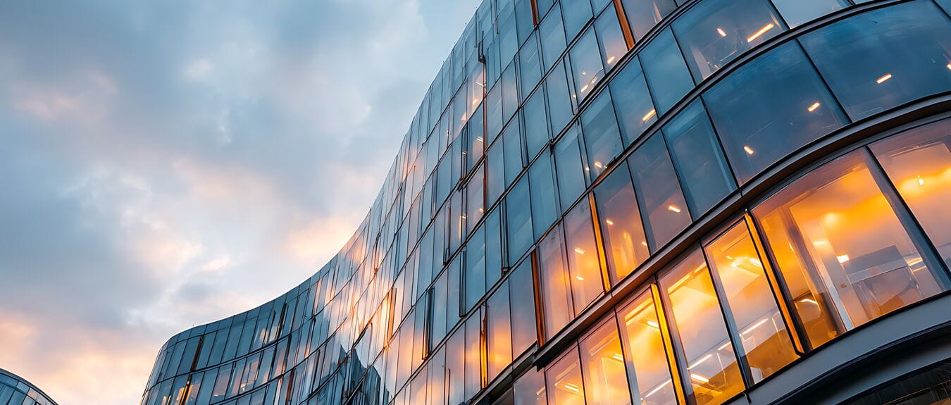 Low angle view of modern glass building reflecting sunset sky with curved architecture design style facade