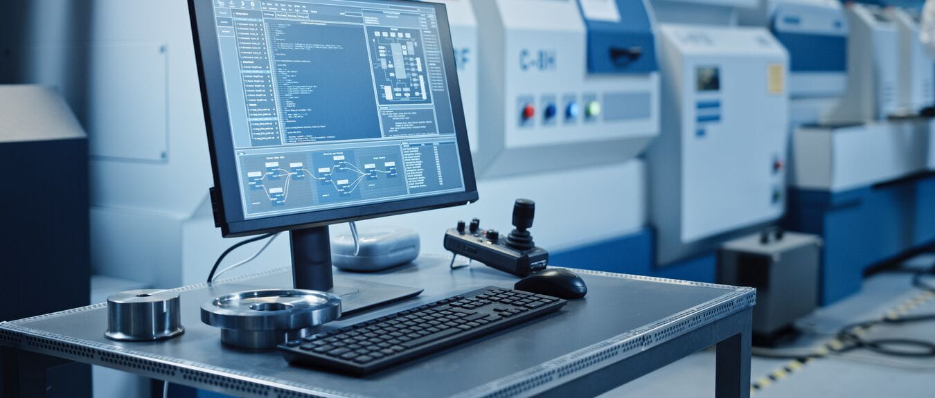 Factory Cleanroom: On the Desk Personal Computer Showing Infrastructure System Control on its Display. In Background CNC Machinery, Professionals Use Robot Arm on Production Line.